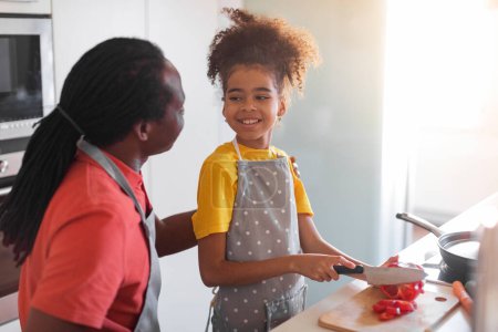 Photo for Cute Black Preteen Girl Helping Father Cooking Lunch In Kitchen, Happy African American Dad And His Preteen Daughter Preparing Healthy Food At Home, Female Child Cutting Bell Pepper, Free Space - Royalty Free Image