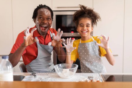 Téléchargez les photos : Cuisine Fun. joyeux noir père et fille tromper ensemble pendant la cuisson, Preteen afro-américaine fille et son père rugissant et grimaçant à la caméra, imitant tigre effrayant tout en cuisinant pâtisserie - en image libre de droit