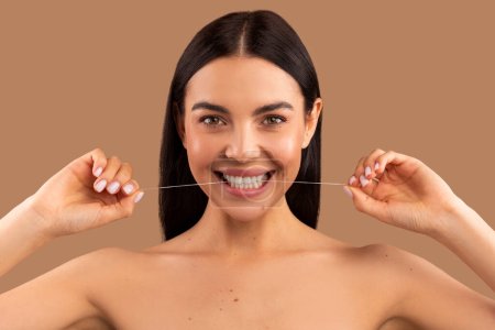 Photo for Headshot of beautiful cheerful brunette long-haired naked woman using dental thread floss and smiling, cleaning teeth after food isolated over beige pastel color background, dental care concept - Royalty Free Image