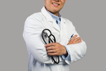 Foto de Terapeuta masculino chino adulto confiado sonriente en bata blanca con estetoscopio, aislado sobre fondo gris, recortado, estudio. Atención de la salud, protección médica y tratamiento, apoyo durante covid-19 - Imagen libre de derechos