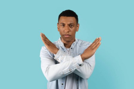 Photo for Sad serious handsome young african american man in casual crossed arms doing stop sign, isolated on blue background, studio. Gesture against racism, violence and covid-19 quarantine, facial expression - Royalty Free Image