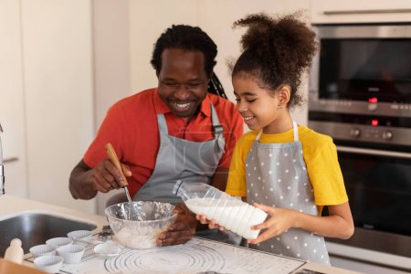 Photo for Happy Black Family Father And Daughter Baking Together In Kitchen. Cute Preteen African American Girl Pouring Milk To Bowl, Adding Ingredients While Preparing Dough For Cookies With Dad At Home - Royalty Free Image
