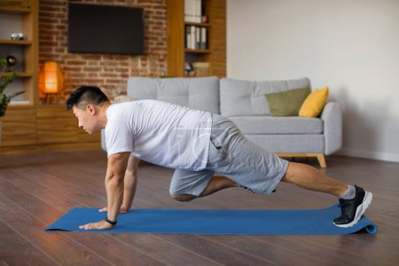 Photo for Active mature asian man doing cross body mountain climbers exercises on fitness mat, training in living room interior, copy space, side view - Royalty Free Image
