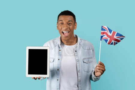 Photo for Cheerful young african american man student with open mouth show England flag, tablet with empty screen isolated on blue background. Recommendations, advice to learn language, app for education remote - Royalty Free Image