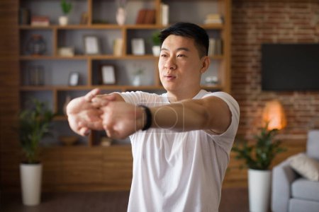 Foto de Hombre asiático maduro estirando las manos, haciendo ejercicio en casa en el interior de la sala de estar, espacio de copia. Hombre coreano de mediana edad que se calienta para el entrenamiento doméstico durante el covidio - Imagen libre de derechos