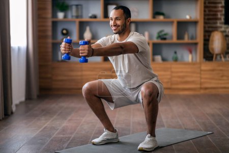 Photo for Portrait Of Happy Young Black Man Making Squats And Training With Dumbbells At Home, Smiling Athletic African American Guy Exercising In Living Room Interior, Enjoying Domestic Workout, Copy Space - Royalty Free Image