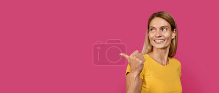 Photo for Smiling mature caucasian blond lady in casual point finger at copy space, isolated on pink background, panorama, studio, close up. Good offer, ad, advice and recommendation from professional blogger - Royalty Free Image