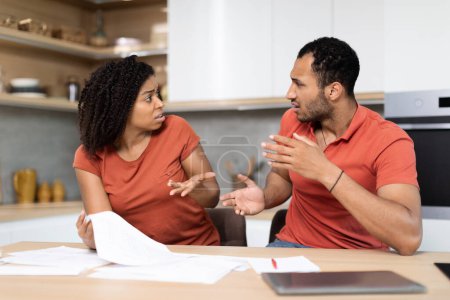 Photo for Upset young black male and woman in red t-shirts work with documents, check bills, quarreling in kitchen interior. People emotions from stress, crisis, debts, credit and mortgage, bookkeeping at home - Royalty Free Image