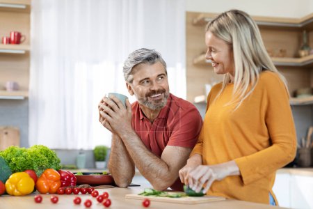 Photo for Positive caucasian family enjoying time together at home, happy middle aged blonde woman and grey-haired man cooking delicious healthy meal at kitchen, cutting organic vegetables, chatting, copy space - Royalty Free Image