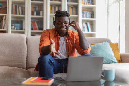 Photo for Happy overweight millennial african american man student sitting on couch at home, using headset and newest laptop, attending webinar or having online lesson, copy space. E-education concept - Royalty Free Image
