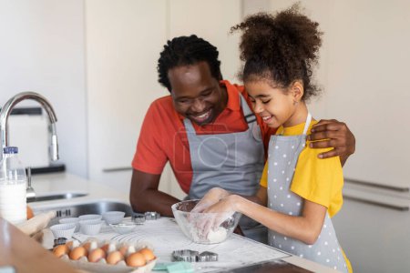 Photo for Cute Black Girl Helping Father While They Baking Together At Home, Preteen African American Female Child Kneading Dough For Cookies In Kitchen, Enjoying Cooking With Her Daddy, Free Space - Royalty Free Image