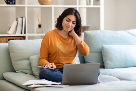 Photo for Young Arab Woman Suffering Neck Pain While Working Or Studying With Laptop Computer At Home, Tired Middle Eastern Female Freelancer Sitting On Couch And Massaging Inflamed Area, Copy Space - Royalty Free Image