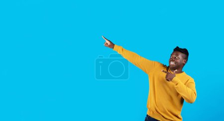 Photo for Crazy Sales. Funny Black Guy Pointing At Copy Space On Blue Background, Cheerful Young African American Man Showing Free Place For Your Advertisement Or Recommending Nice Offer, Panorama - Royalty Free Image