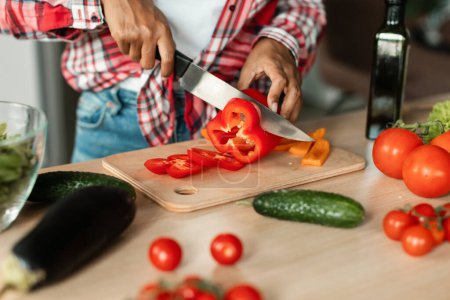 Photo for Millennial black female chef preparing salad, cut pepper, prepare lunch at table with organic vegetables in kitchen interior, close up, cropped. Health care, vegan food, proper nutrition at home - Royalty Free Image