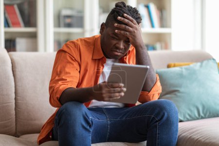 Photo for Anxious african american young man feel down, receive bad unexpected message on digital tablet, frustrated chubby black guy disappointed by problems with business, reading news online at home - Royalty Free Image