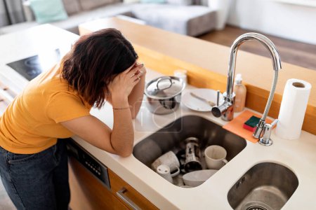 Photo for Domestic Chores Stress. Depressed Housewife Looking At Pile Of Dirty Dishes In Sink, Desperate Young Woman Touching Head And Leaning At Kitchen Counter, Tired Of Cleaning At Home, Above View - Royalty Free Image