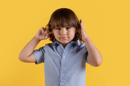 Photo for Hear no evil. Stubborn little boy closing his ears with fingers, doesnt want to listen, looking at camera, orange studio background - Royalty Free Image