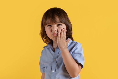 Photo for Kids dental care concept. Cute little boy suffering from acute tooth pain, touching his painful cheek and frowning face, orange studio background, free space - Royalty Free Image