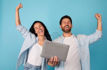 Photo for Satisfied emotional young european couple with laptop make gesture of success and victory, enjoy win together, isolated on blue background, studio. Reaction to great news, huge sale, ad and offer - Royalty Free Image