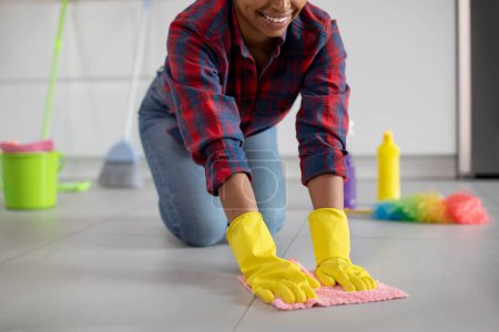 Foto de Sonriente millennial africana americana ama de casa en guantes de goma lava el piso en el interior de la cocina, de cerca, recortado. Servicio de limpieza, pureza perfecta, lucha con tareas sucias y domésticas en casa - Imagen libre de derechos