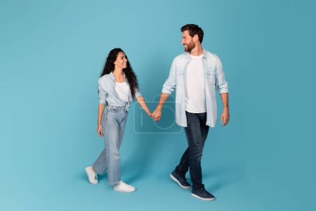 Photo for Cheerful handsome young european bearded guy leads the hand of lady in casual, isolated on blue background, studio, full length. Couple enjoy free time, walk together, offer and ad, love and romance - Royalty Free Image