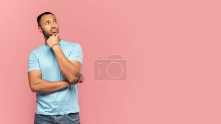 Foto de Pensativo hombre afroamericano pensando y tocando la barbilla, mirando a un lado en el espacio de copia, posando sobre fondo rosa, filmado en el estudio. Déjame pensar concepto - Imagen libre de derechos