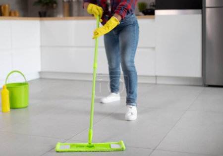 Photo for Millennial african american lady in rubber gloves with bucket and mop washes floor, enjoys household chores in minimalist kitchen interior, cropped, close up. House cleaning alone and cleaning service - Royalty Free Image
