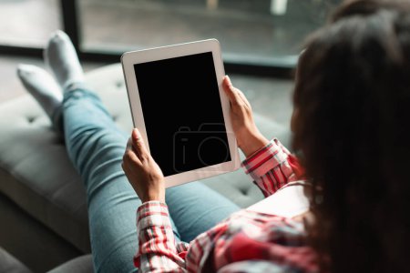 Photo for New app for chat. Millennial black female using tablet with blank screen, ordering goods remotely, checking account, watch video in living room interior. Online shopping, big sale and meeting at home - Royalty Free Image