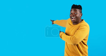 Photo for Look There. Amazed Black Man Pointing At Copy Space Behind Him, Cheerful Young African American Male Demonstrating Free Empty Place On Blue Background For Advertisement Design, Panorama - Royalty Free Image