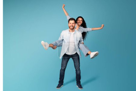 Photo for Cheerful young european guy hold woman in casual on back, have fun, isolated on blue background, studio, full length. Couple enjoy free time together, success and victory emotions, great offer and ad - Royalty Free Image