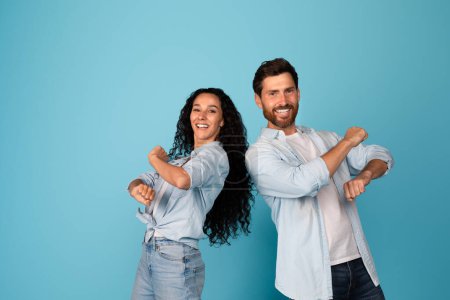 Photo for Cheerful young european male and arab female in casual have fun together, dance, couple enjoy free time and victory, isolated on blue background, studio. Entertainment and lifestyle, offer and ad - Royalty Free Image