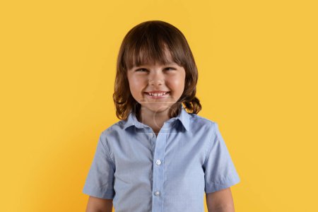 Foto de Concepto de felicidad para niños. Primer plano retrato de lindo niño sonriendo ampliamente a la cámara, posando sobre fondo de estudio naranja - Imagen libre de derechos