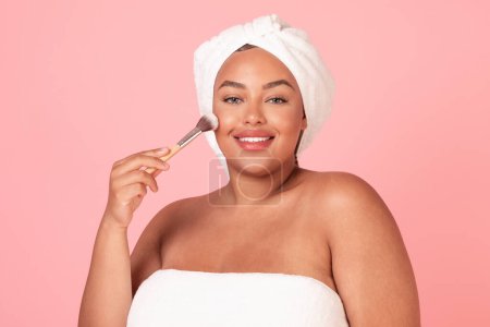 Photo for Makeup concept. Beautiful black body positive woman holding makeup brush, doing contouring or applying blush on face isolated on pink studio background - Royalty Free Image