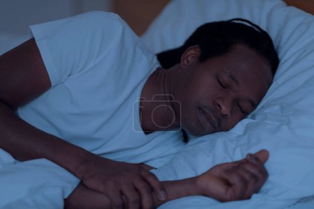 Photo for Closeup Portrait Of Young African American Man Sleeping In Bed During Night Time, Calm Handsome Black Male Lying On Soft Pillow With Eyes Closed, Napping While Resting In Bedroom At Home - Royalty Free Image