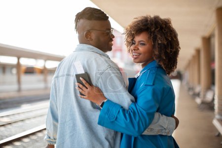 Téléchargez les photos : Portrait Of Happy Black Couple Embracing At Railway Station, Smiling Romantic African American Spouses Standing On Platform And Waiting For Train, Enjoying Travelling Together, Free Space - en image libre de droit
