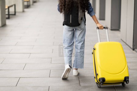 Foto de Vista trasera de la mujer en traje casual que tiene viaje al extranjero, caminando por el aeropuerto moderno con equipaje amarillo, llevando mochila, panorama con espacio de copia, recortado. Viajar, concepto de vacaciones - Imagen libre de derechos