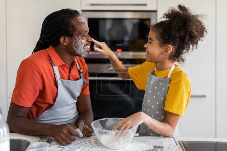 Téléchargez les photos : Cheerful Black Dad And Daughter Playing With Floor While Baking Together In Kitchen, Happy African American Father And Preteen Female Child Having Fun And Enjoying Cooking At Home, Closeup - en image libre de droit