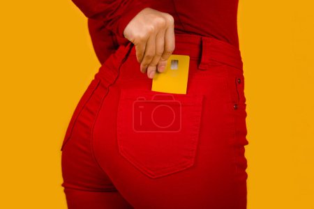 Photo for Close up cropped photo shot of female hand arm putting credit bank card in red jeans pants denim back pocket isolated on orange studio background. Money finance currency concept - Royalty Free Image