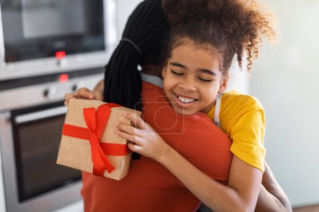 Téléchargez les photos : Fathers Day Concept. Happy Preteen Black Girl Embracing Dad And Holding Gift Box, Joyful Female Child Surprising Her Daddy With Present While They Bonding Together At Home, Closeup Shot - en image libre de droit