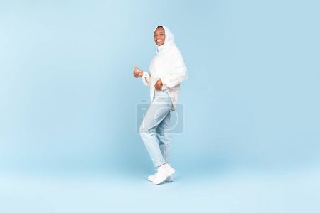 Téléchargez les photos : Happy african american woman in hijab showing thumb up and smiling at camera, posing on blue background, full length shot, copy space for advertisement - en image libre de droit