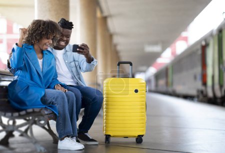 Téléchargez les photos : Happy Black Couple At Railway Station Celebrating Success With Smartphone, Overjoyed African American Spouses Sitting On Bench, Holding Mobile Phone And Exclaiming With Excitement, Copy Space - en image libre de droit