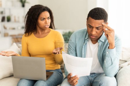 Photo for Angry unhappy millennial african american lady quarreling at guy over debts and bills with laptop in living room interior. People emotions, problems with finances, bankruptcy, taxes and crisis at home - Royalty Free Image