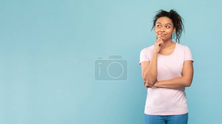 Foto de Thoughtful african american woman thinking and looking aside at free space, posing standing on blue studio background, panorama. Let me think about it concept - Imagen libre de derechos