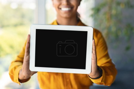 Téléchargez les photos : Happy black businesswoman holding digital tablet with blank screen posing in office interior, free space, mockup. Recommendation of new business app and website - en image libre de droit