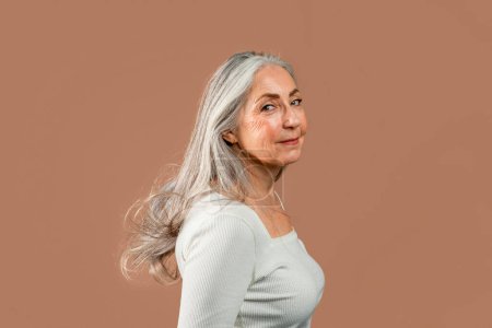 Photo for Cheerful old caucasian female with natural makeup, gray hair looks at camera, enjoy beauty and freedom, isolated on brown background, studio. Skin care, anti-aging treatments, lifestyle and spa day - Royalty Free Image