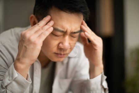 Photo for Closeup of asian middle aged man suffering from headache, touching his temples, sitting with closed eyes, copy space. Migraine, headache, stress, tension problem, hangover concept - Royalty Free Image