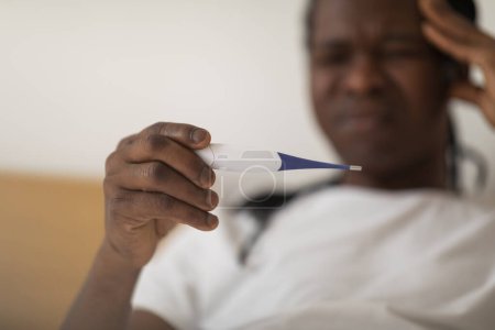 Photo for Closeup Of Sick Black Man Holding Thermometer And Touching Head, Ill Young African American Male Having Fever, Suffering High Temperature And Feeling Unwell At Home, Selective Focus - Royalty Free Image
