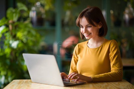 Photo for Concentrated at work, women in business. Confident cheerful young brunette woman in smart casual wear working on modern laptop while sitting at table in creative office or cafe, copy space - Royalty Free Image