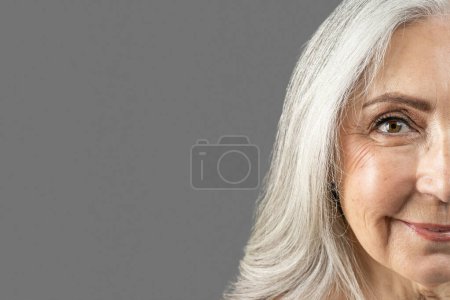 Téléchargez les photos : Smiling elderly european woman after anti-aging treatment look at camera, isolated on gray background, studio, close up. Anti wrinkles skin care, beauty procedures, ad and offer, result before, after - en image libre de droit