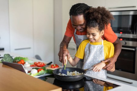 Téléchargez les photos : Caring Black Dad Teaching His Preteen Daughter Cooking Food At Home, Happy African American Family Father And Female Child Preparing Lunch Together In Kitchen, Making Meal In Pan, Copy Space - en image libre de droit